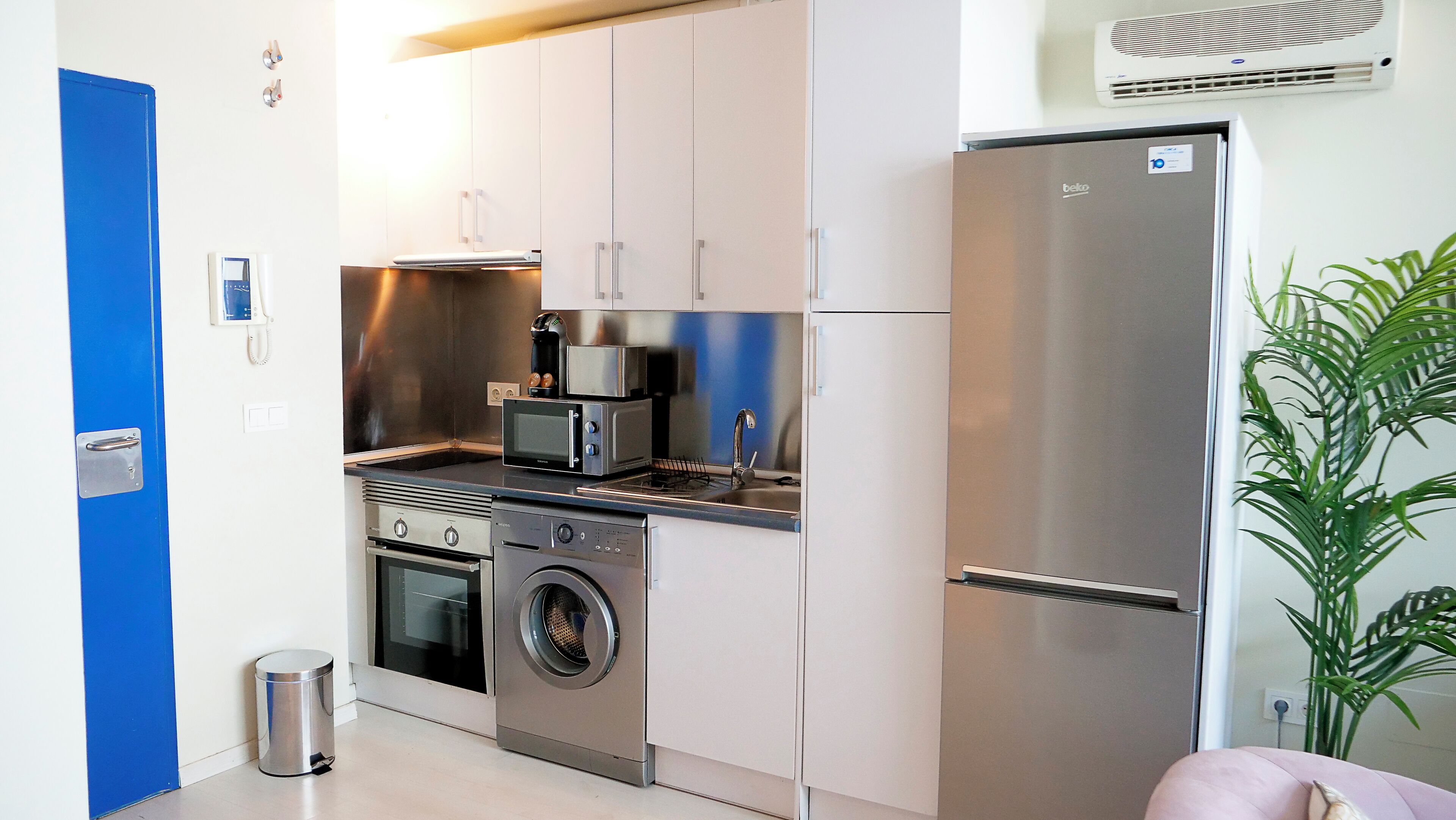 A compact kitchen with a built-in oven, microwave, coffee maker, and a washing machine.
