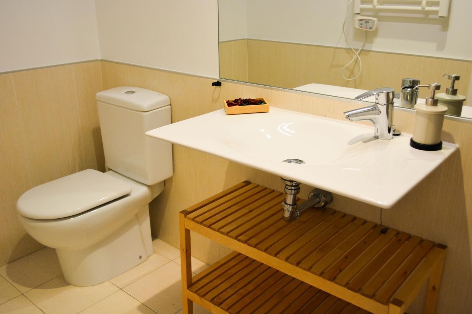 A bathroom with a toilet, a sink, and a wooden shelf.
