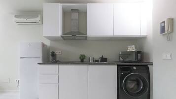 Una cocina compacta con armarios blancos, microondas integrado, lavadora y cafetera.