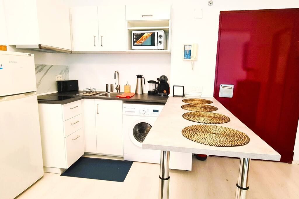 A compact kitchen with white cabinets, a microwave, a coffee maker, and a washing machine.