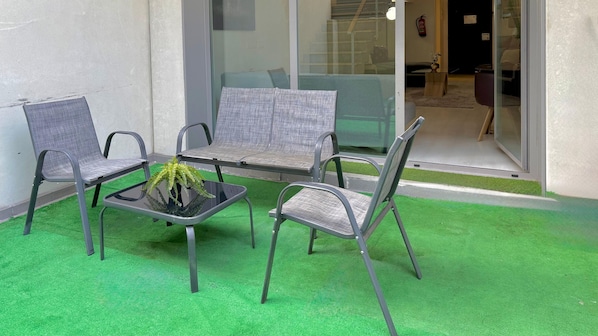 Un área de estar con cuatro sillas y una mesa, una planta en maceta y una puerta de vidrio que da a un espacio interior.