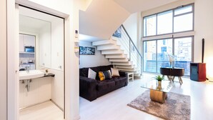 A modern living room with a staircase, a sofa, a coffee table, and a view of the city through large windows.