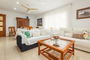 Un salon comprenant un canapé, une table basse, une table à manger avec des chaises, un ventilateur de plafond et un tableau accroché au mur.