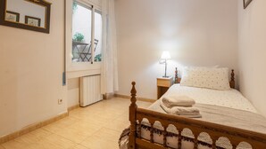 Un dormitorio con cama, mesita de noche con lámpara, ventana con cortinas y radiador.