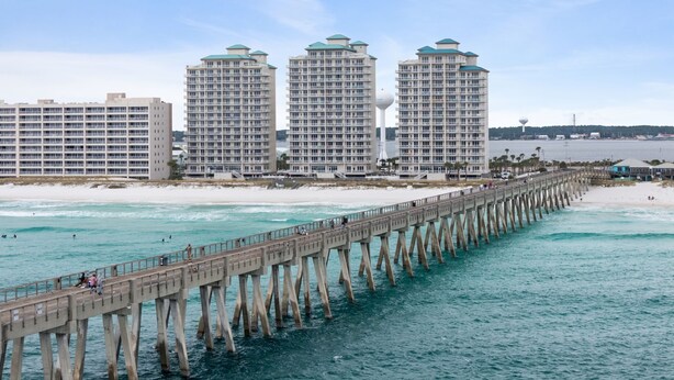 Un muelle costero se adentra en el océano, con edificios altos al fondo.