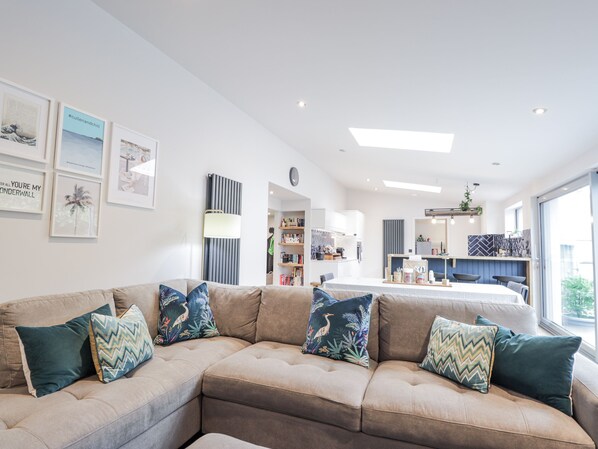 A modern living room with a sectional sofa, a kitchen area, and a dining space. - Apple Tree Cottage (Buckie)
