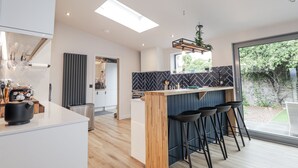 A modern kitchen with a central island, bar stools, and a view of the outdoors. - Apple Tree Cottage (Buckie)