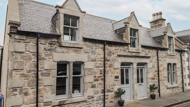 A stone building with a gabled roof, multiple windows, and a door. - Apple Tree Cottage (Buckie)