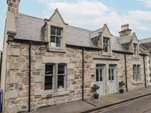 A stone building with a gabled roof, multiple windows, and a door. - Apple Tree Cottage (Buckie)