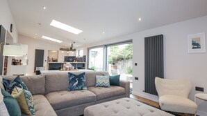 A modern living room with a sectional sofa, a chair, and a dining area with a kitchen in the background. - Apple Tree Cottage (Buckie)