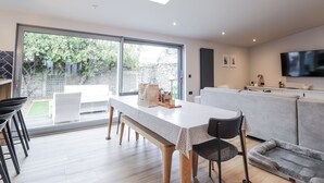A modern kitchen with a large island, a dining area with a table and chairs, a grey sofa, and a TV mounted on the wall. - Apple Tree Cottage (Buckie)