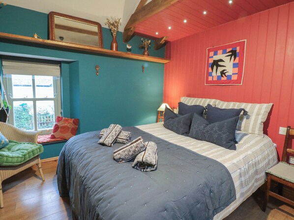 Une chambre à coucher avec un grand lit, une chaise, une fenêtre et un mur orné d’un tableau.