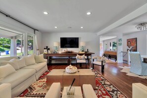 A spacious living room with a large sofa, a coffee table, and a dining area with a TV and table lamps. - Parkside Blue-Walkable to Downtown & UofA-Sauna (Fayetteville)