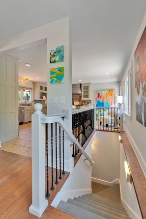 A staircase with a white balustrade, a kitchen area with cabinets, and a dining area with a table and chairs. - Parkside Blue-Walkable to Downtown & UofA-Sauna (Fayetteville)