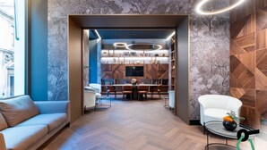 A modern interior with a herringbone wood floor, a white sofa, a dining area with a table and chairs, and a kitchen with wooden cabinets and a large window. - Hotiday Roma Trevi (Rome)