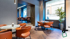 A modern restaurant with orange chairs, marble tables, and a large window with a view of a building. - Hotiday Roma Trevi (Rome)