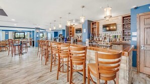 A bar area with wooden chairs and a bar counter, featuring hanging pendant lights and a television. - Cozy 1-Bedroom Oceanfront Condo in Myrtle Beach (Myrtle Beach)