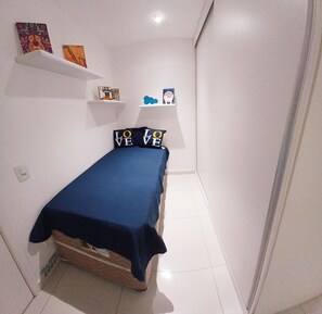 A small, neatly arranged bedroom with a bed, a shelf with decorative items, and a wall-mounted light fixture. - Balcony with a view of the ocean   (Rio de Janeiro)