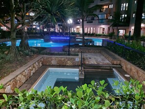 A swimming pool area with stone steps leading into the water, surrounded by greenery and palm trees. - Balcony with a view of the ocean   (Rio de Janeiro)