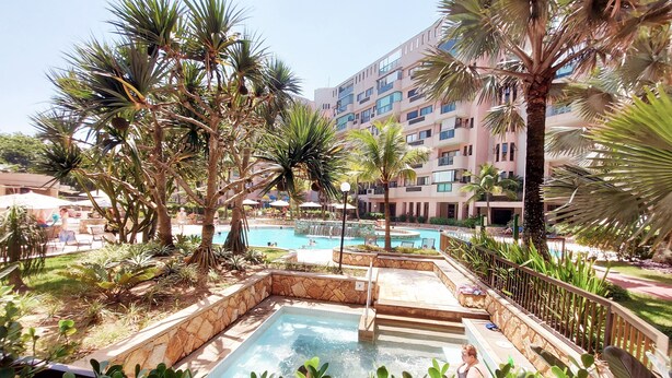 Un área de piscina con un jacuzzi, rodeado de palmeras y un edificio al fondo.