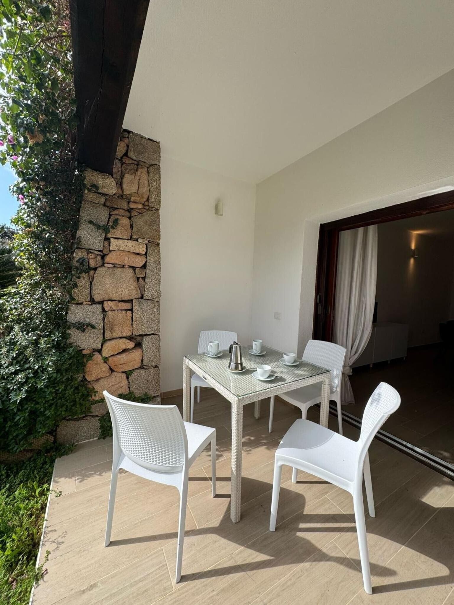 Un patio con muro de piedra, una mesa con sillas y vista al interior.