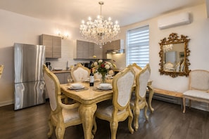 A dining area with ornate chairs, a chandelier, and a modern kitchen in the background.