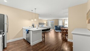 Une cuisine moderne avec un îlot central, un coin repas avec une table et des chaises en bois, un salon avec un canapé et une vue sur le balcon.
