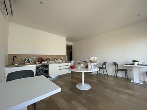 A modern kitchen with a dishwasher, a sink, and a countertop with various items. There is a dining area with a white table and chairs. - Room 'Camera Deluxe' with Wi-Fi and Air Conditioning (Olbia)