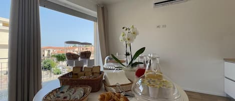 A breakfast buffet with pastries, bread, and beverages on a table in a hotel room with a view.