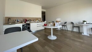 Una cocina moderna con lavavajillas, un lavabo y una encimera con varios objetos. Hay un comedor con una mesa y sillas blancas.