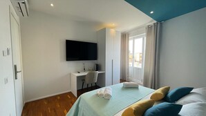 Una habitación de hotel con cama, escritorio, televisor y ventana con cortinas.