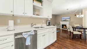A modern kitchen with white cabinetry, a stainless steel sink, and a dining area with a fireplace. - Big-Group Lock-Off Condo | 1BR + Resort Room | Sleeps a Crowd (York)