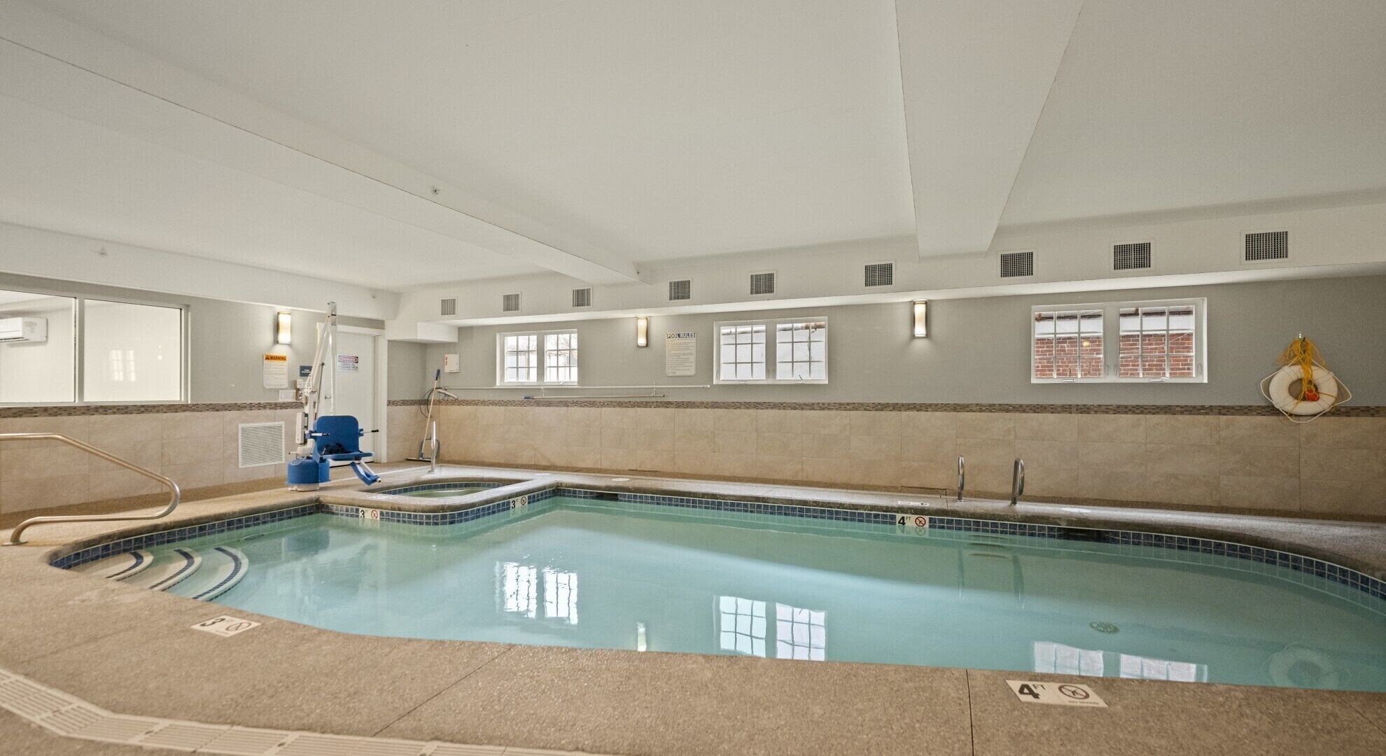 An indoor swimming pool with clear water, a blue chair, and a lifebuoy on the wall.