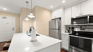 Une cuisine moderne avec des meubles blancs, des appareils en acier inoxydable, un îlot central doté d’un évier et des luminaires suspendus.