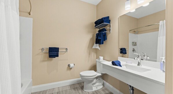 A modern bathroom with a beige wall, a white toilet, a sink with a mirror, and a towel rack with blue towels.