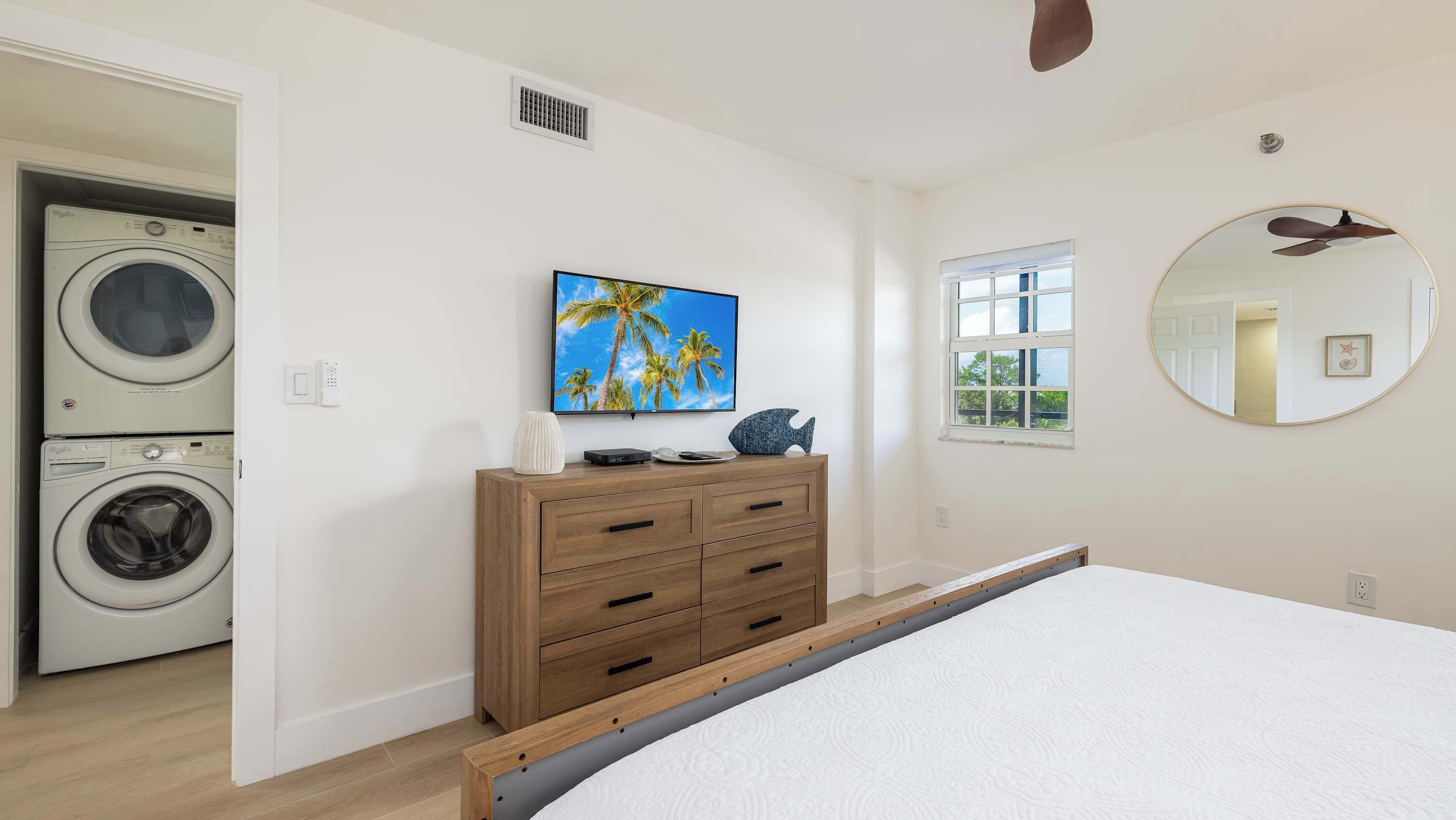Un dormitorio con cama, cómoda, televisor, ventana y lavadora.