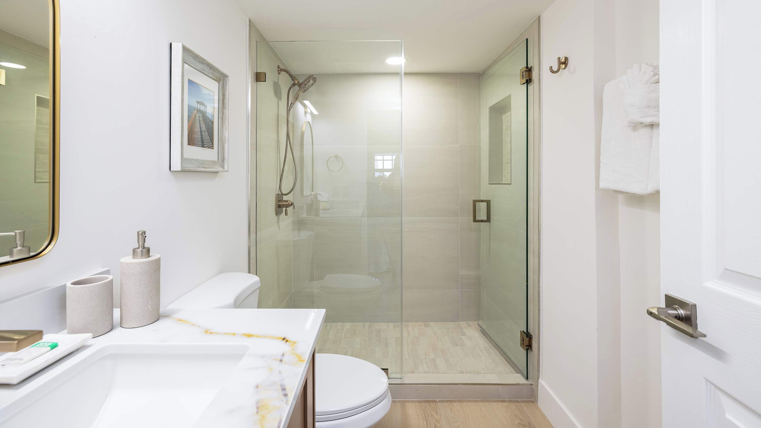 A modern bathroom with a glass-enclosed shower, a toilet, and a sink with marble countertops.