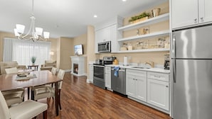 A modern kitchen with white cabinets, stainless steel appliances, and a dining area with a wooden table and chairs. - 1-Bedroom Coastal Retreat Near Nubble Lighthouse (York)