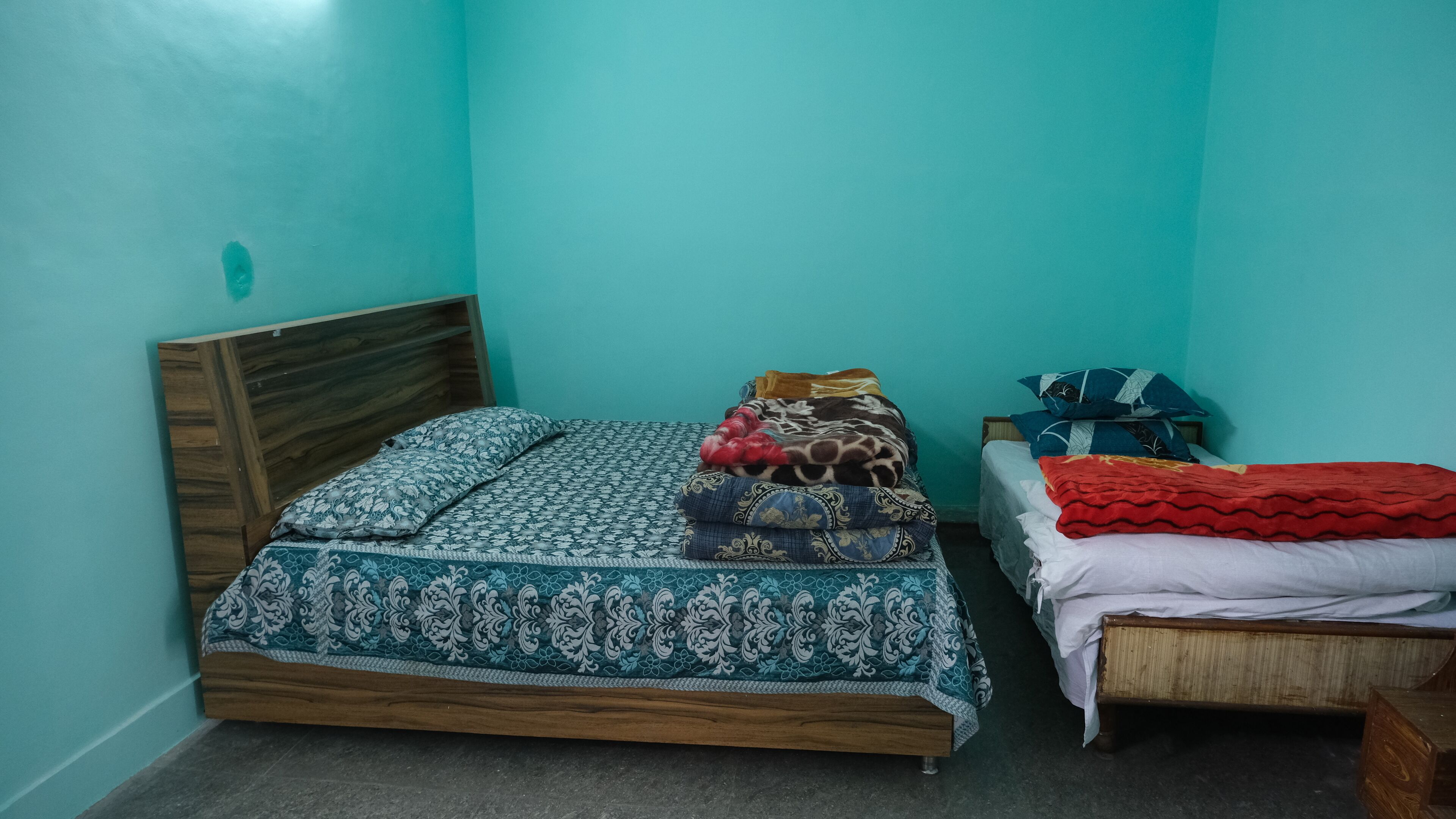 A small room with two beds, one with a patterned bedspread and the other with a red blanket.