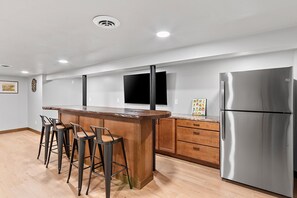 A modern kitchen with a stainless steel refrigerator, wooden bar stools, and a flat-screen TV mounted on the wall. - 4-bedroom house in Titletown (Ashwaubenon)