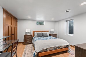 Ein Schlafzimmer mit einem Bett, Nachttischen, einem Schreibtisch, einem Sessel, einem Kleiderschrank, einem Fenster und einer Deckenleuchte.