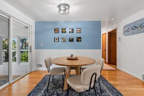 Ein Essbereich mit einem runden Tisch, vier Stühlen, einer blauen Wand mit gerahmten Bildern und einer Deckenleuchte.