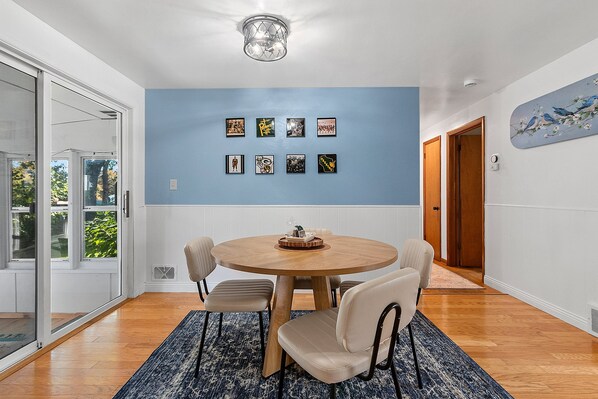 Un coin repas comprenant une table ronde, quatre chaises, un mur bleu orné de tableaux encadrés et un luminaire au plafond.