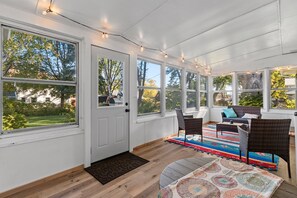 Une véranda avec de grandes fenêtres, une porte, des meubles en osier et un tapis à motifs.