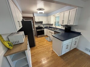 A kitchen with white cabinets, a black refrigerator, stainless steel appliances, and a wooden floor. - 4-bedroom house in Titletown (Ashwaubenon)