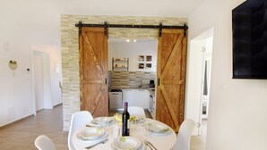 A dining area with a white table set for four, a kitchen in the background, and a sliding barn door entrance. - Relaxing Holiday Home With Shared Pool (Umag)