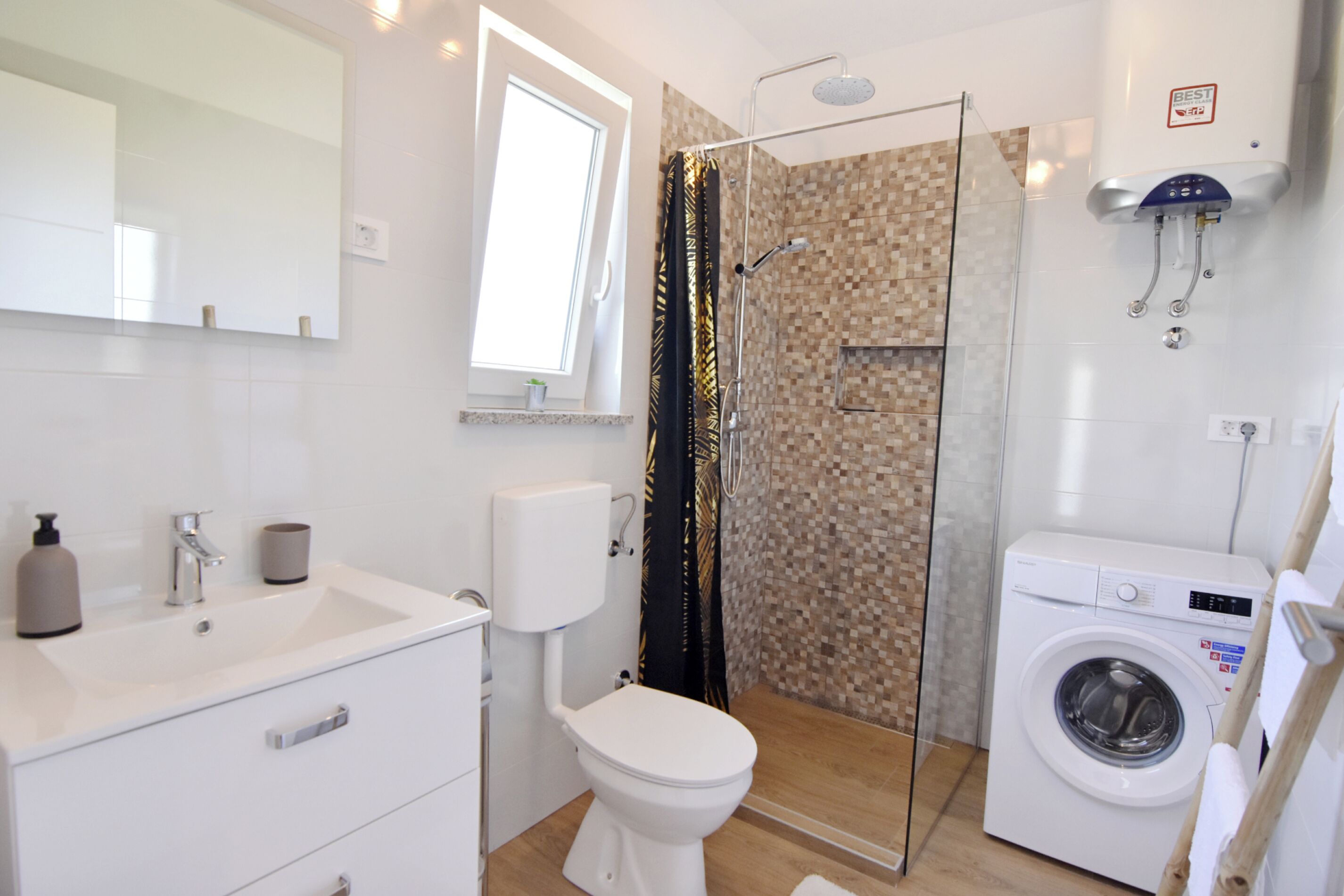 A modern bathroom with a toilet, sink, shower, and washing machine.