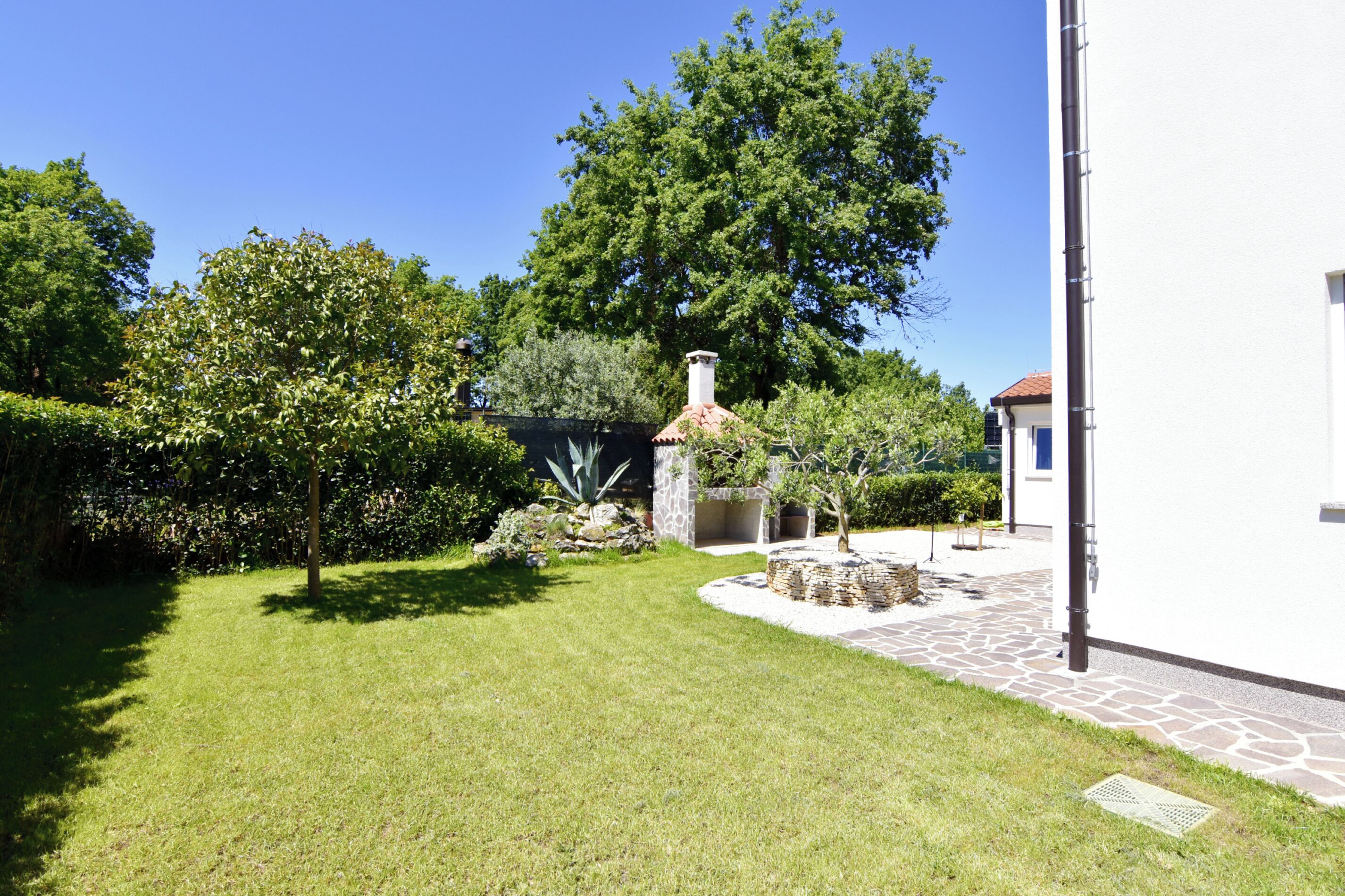 A well-maintained garden with a stone pathway, a large tree, and a white building with a red roof.