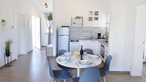 A modern kitchen with white cabinets, a built-in oven, and a dining area with a round table and blue chairs. - Modern Holiday Home With Shared Pool (Umag)