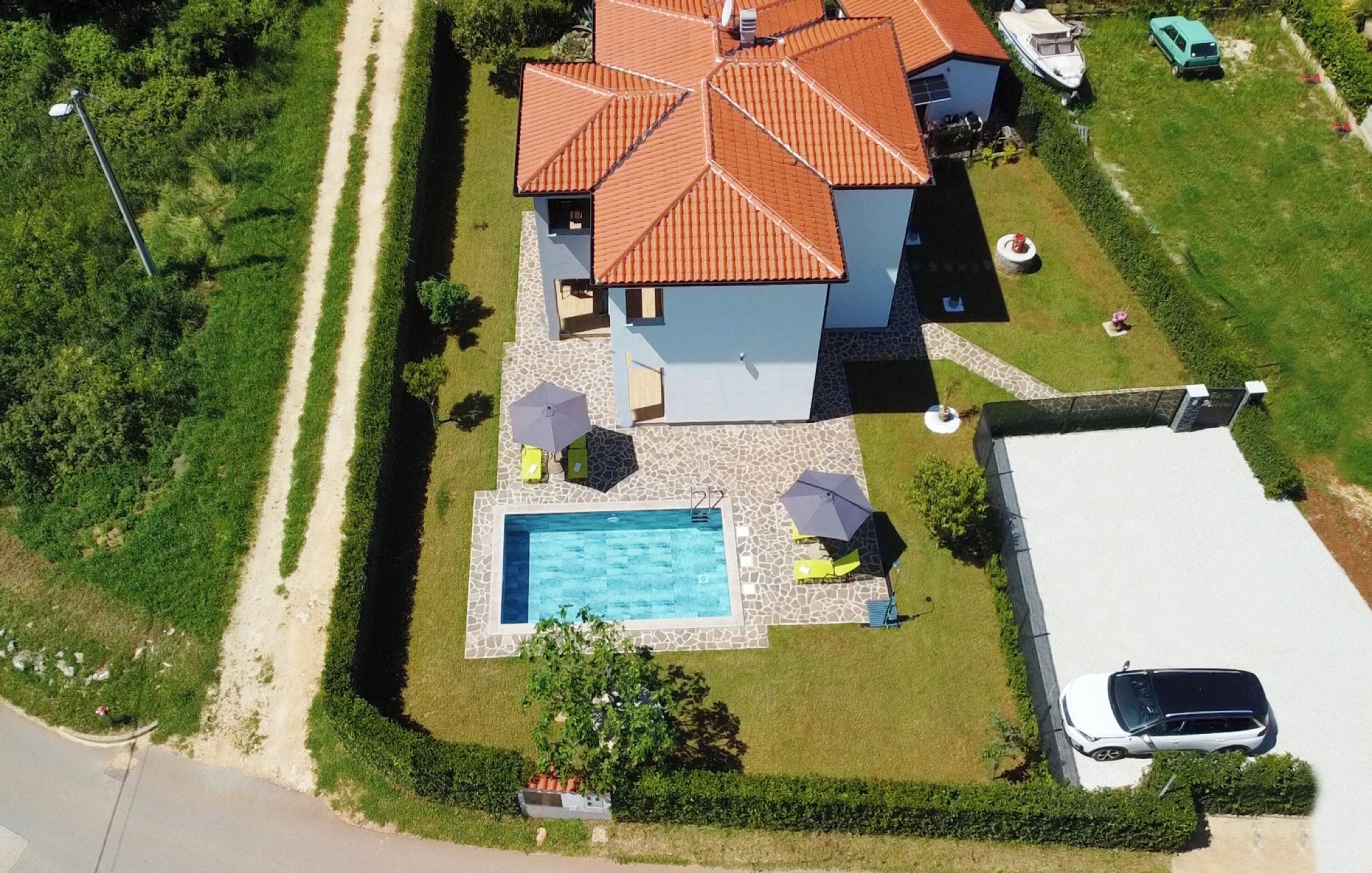 An aerial view of a house with a swimming pool, a covered patio, and a carport.